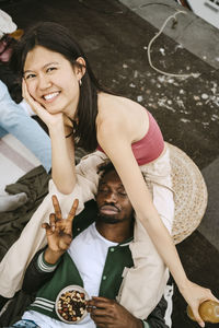 Portrait of happy young woman with male friend gesturing peace sign during rooftop party