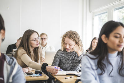 Female students discussing over book at desk in classroom