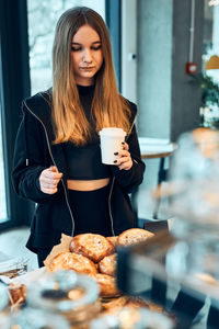 Woman holding cup with coffee looking at pastry, buns, cakes and cookies and waiting for the order