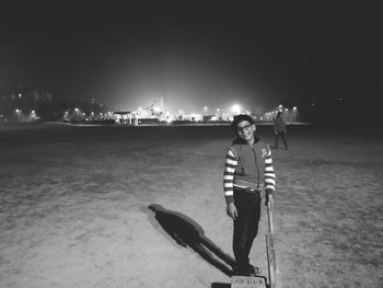Portrait of smiling boy holding cricket bat while standing on field at night