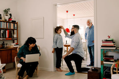 Family looking at man measuring daughter's height against wall at doorway
