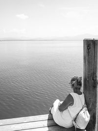 Rear view of woman sitting by lake chiemsee against sky and bavarian alps