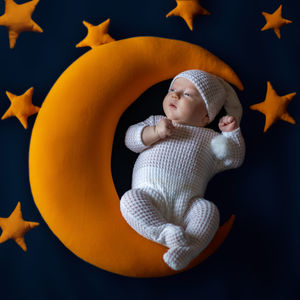 Cute baby sleeps on a moon surrounds by stars