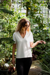 Young woman standing amidst plants in greenhouse