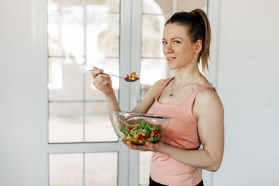 Portrait of an attractive woman holding a salad bowl and looking at the camera. 
