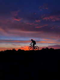 Silhouette man riding bicycle against sky during sunset