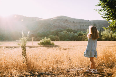 Rear view of girl standing on grassy field against mountain