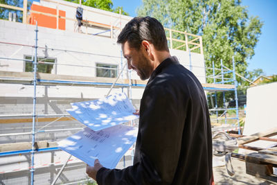 Businessman reading blueprints while standing at construction site on sunny day