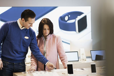 Salesman assisting customer in buying smart watch at store