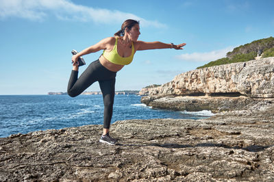 Full length of woman standing on rock against sea and sky