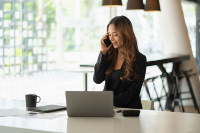Young woman using mobile phone while sitting on table