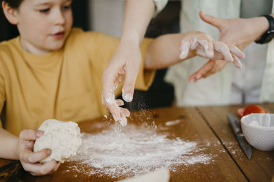 Mother helping son to knead dough on table