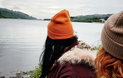 Rear view of women sitting by lake against sky