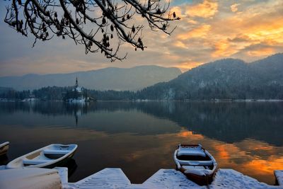 Boats moored at lake by mountains against sky during winter