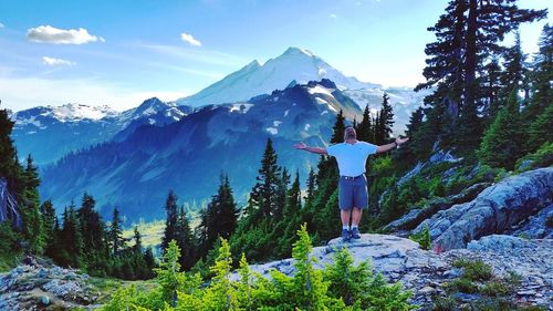 Man with arms outstretched standing on rocks against snowcapped mountains