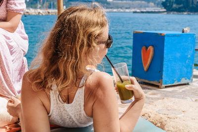 Rear view of young woman relaxing on beach, drinking refreshing matcha latte