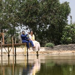 People sitting by lake against trees