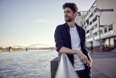 Man standing on bridge over river against sky in city