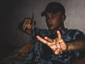 Young man smoking cigarette against wall