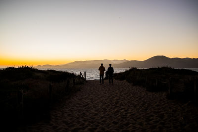 Silhouette people on beach against clear sky during sunset