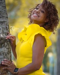 Portrait of smiling woman standing by tree trunk