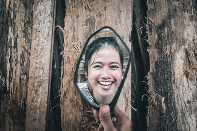 Portrait of a smiling young woman against tree trunk