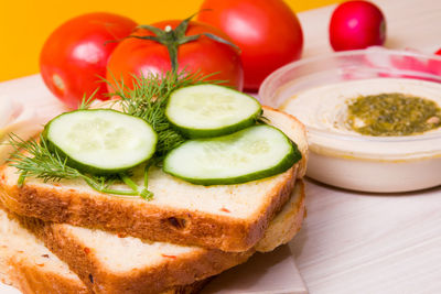 Sliced cucumber on sliced bread, vegetables and a bowl with hummus proper nutrition concept