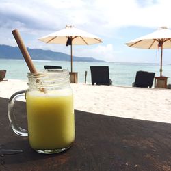 Close-up of drink on table at beach against sky