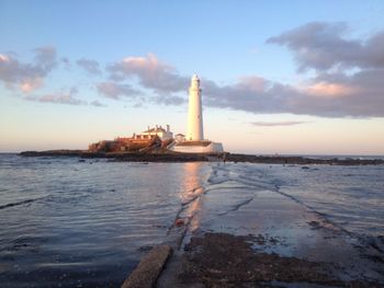 View of lighthouse in sea against cloudy sky