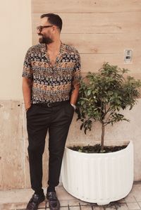 Young man looking away while standing on potted plant against wall