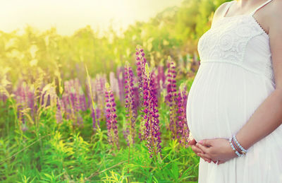 Midsection of pregnant woman standing amidst flowers