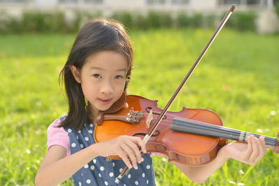 Portrait of girl playing violin on grassy field at public park