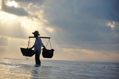 Silhouette man in sea against sky during sunset