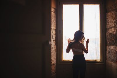 Rear view of woman looking through window at home