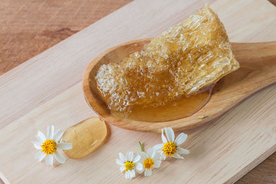 High angle view of honey in spoon on cutting board over wooden table