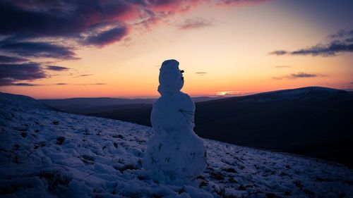 Snowman standing on snow covered land during sunset