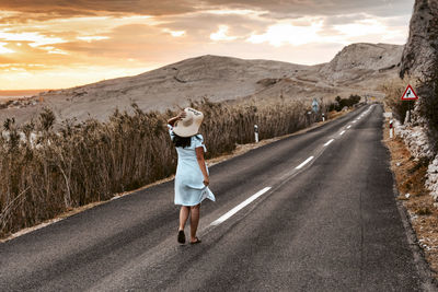 Rear view of woman on road against sky during sunset