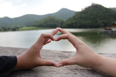 Cropped image of man and woman making heart shape by lake