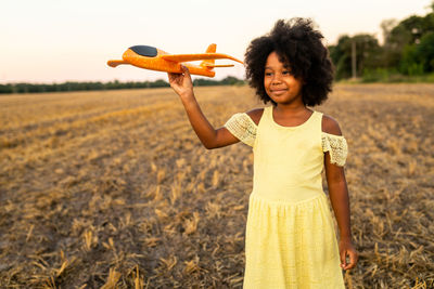 Cute girl holding toy plane on field