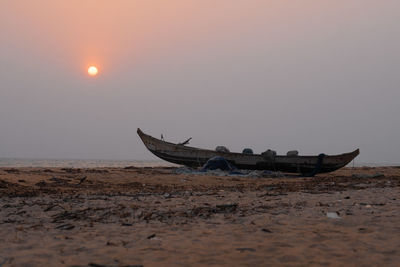 Boat moored on shore against sky during sunset