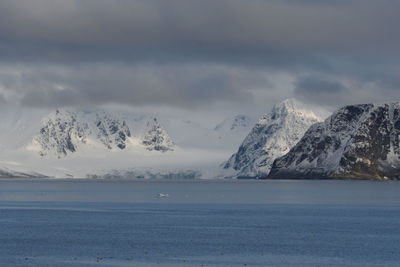 Scenic view of sea by snowcapped mountains against sky