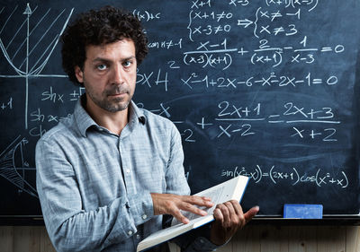 Portrait of teacher standing by blackboard