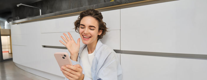 Portrait of young woman using mobile phone while standing at home