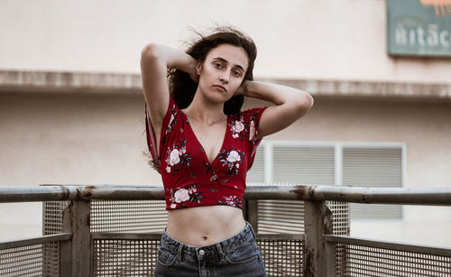 Portrait of young woman with hand in hair standing against railing