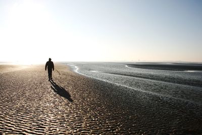 Rear view of silhouette man walking at beach against clear sky during sunset