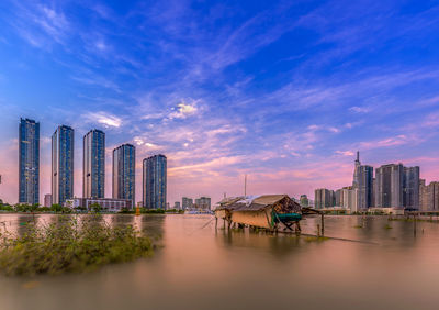 Scenic view of river by buildings against sky during sunset