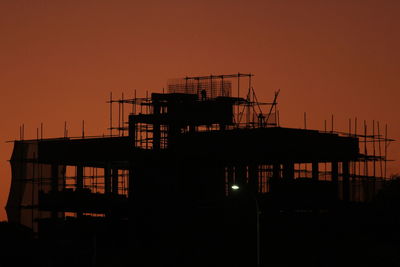 Silhouette built structure on pier against orange sky at sunset