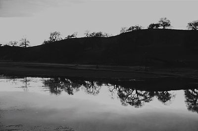 Reflection of silhouette trees in lake against sky