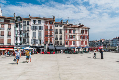 People walking by buildings in city against sky