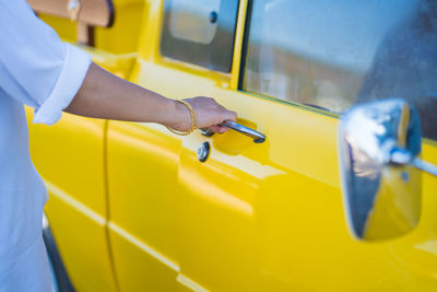 Pretty woman opens door of vintage yellow car standing on city street closeup. 